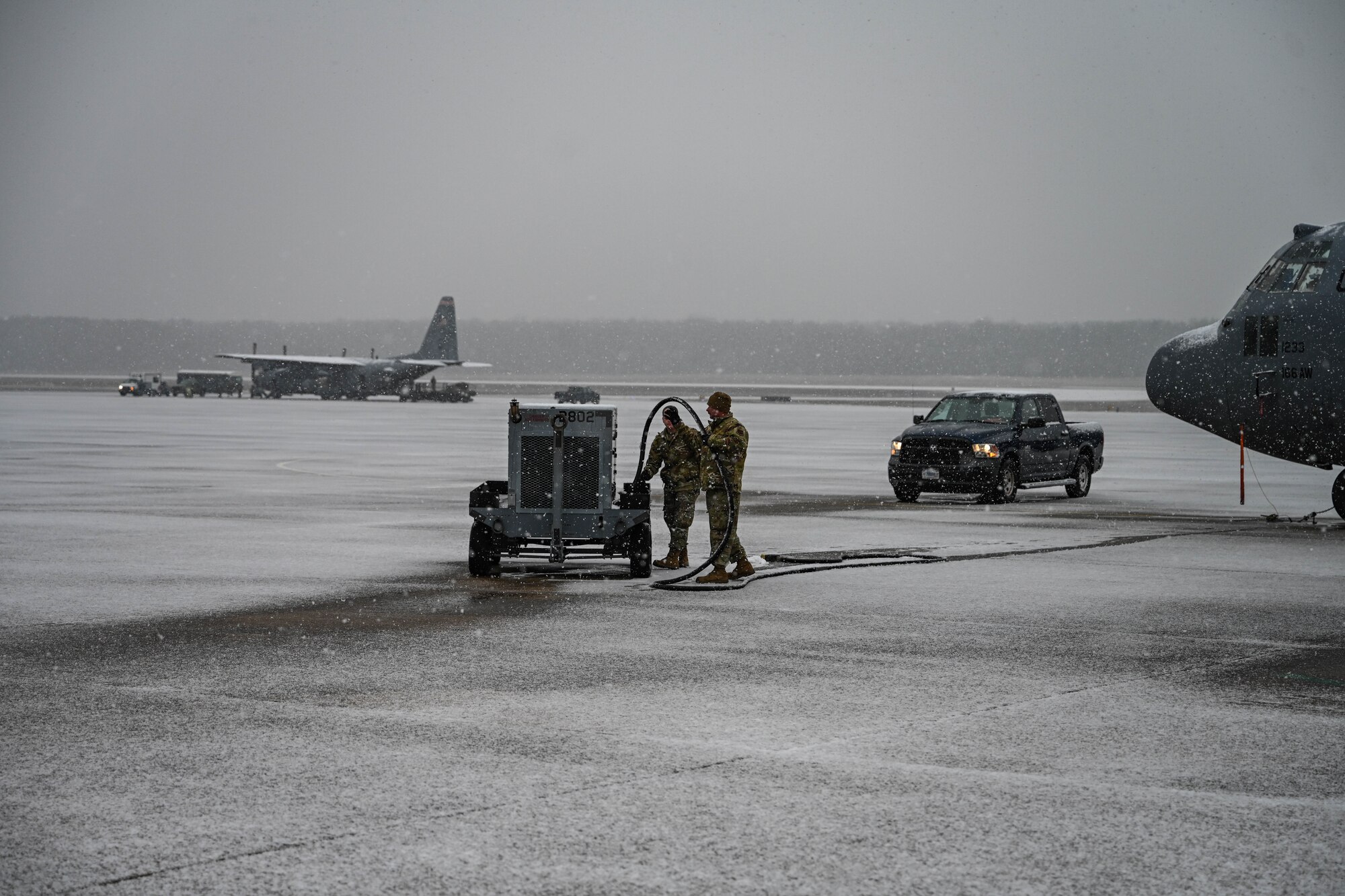 Two people in uniform carry a hose under snowfall.