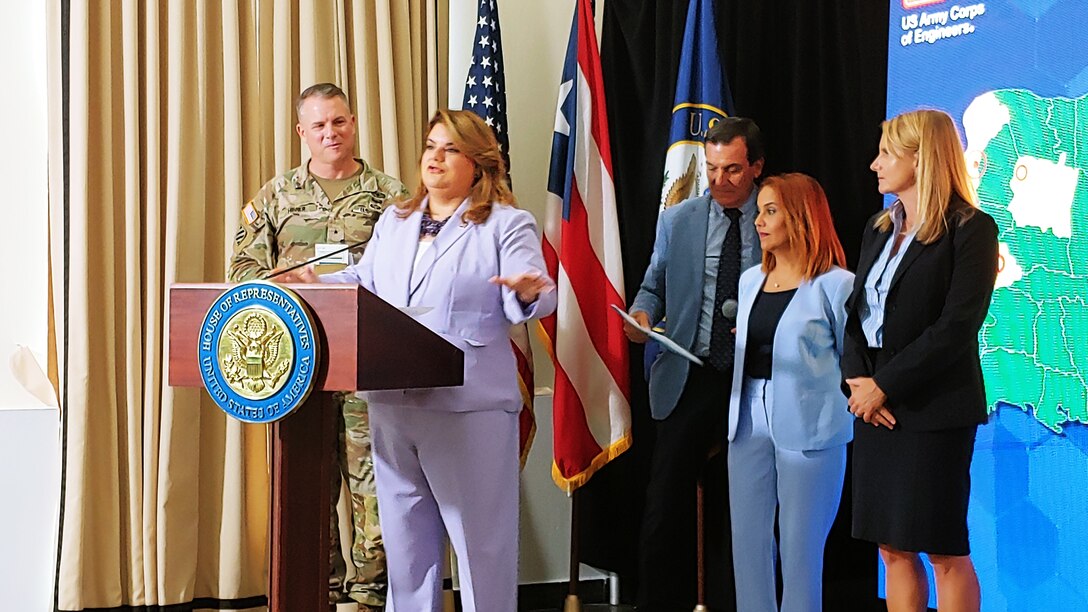 Congresswoman Jenniffer Gonzalez-Colon dressed in a lavender pantsuit behind a podium with Brig. Gen. Daniel Hibner dressed in camouflage standing to her right.