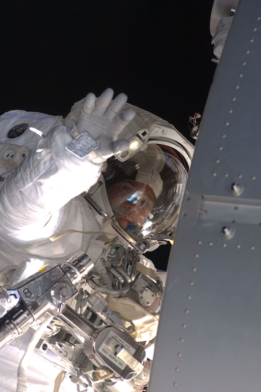 A person in a spacesuit floating in space waves.