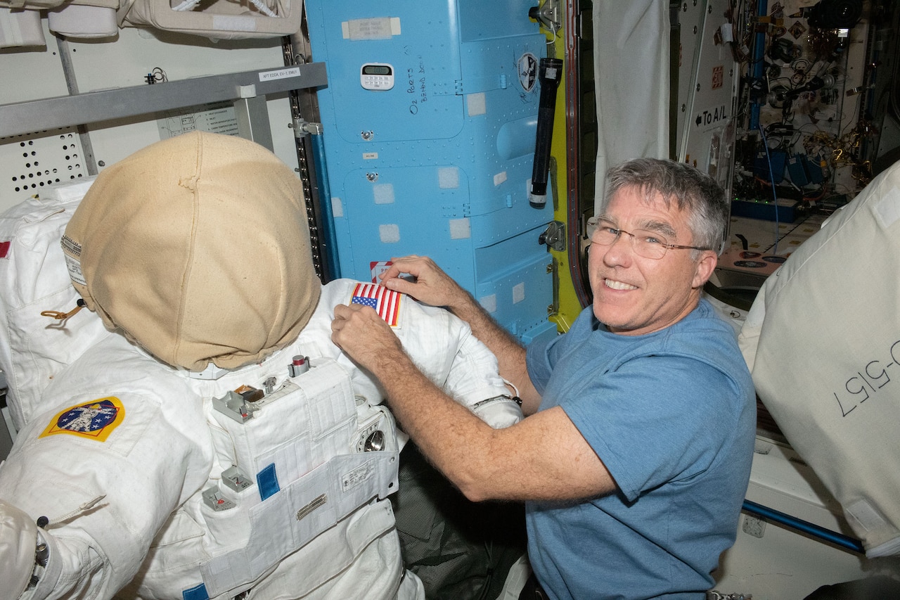 A person putting a U.S. flag patch on a spacesuit smiles for a photo.