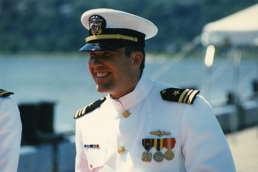 A person in a dress uniform and cap smiles.