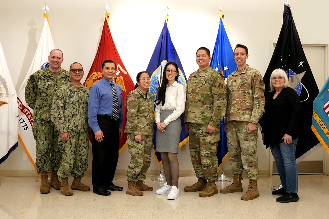 military and civilian men and women stand in front of flags