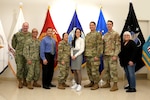 military and civilian men and women stand in front of flags