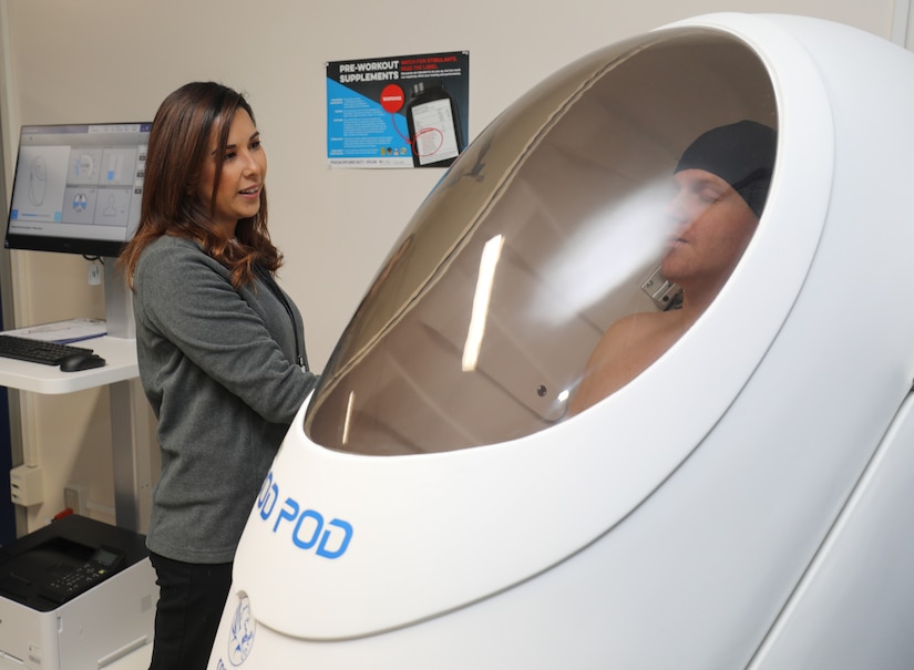 A person watches as another sits in a bod pod.