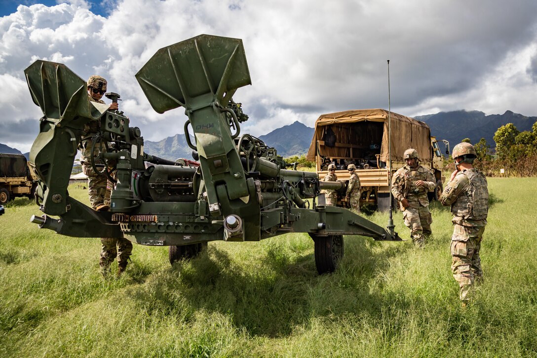 A group of soldiers work in a field with a truck and a large piece of equipment.