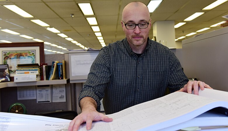 Man looks down at large pieces of paper, indoors.