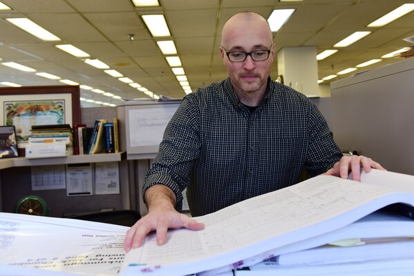 Man looks down at large pieces of paper, indoors.