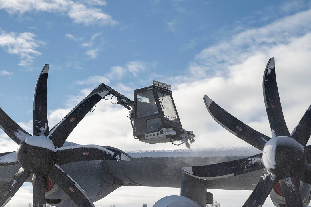 An airman maneuvers a lift over a snow-covered military aircraft.