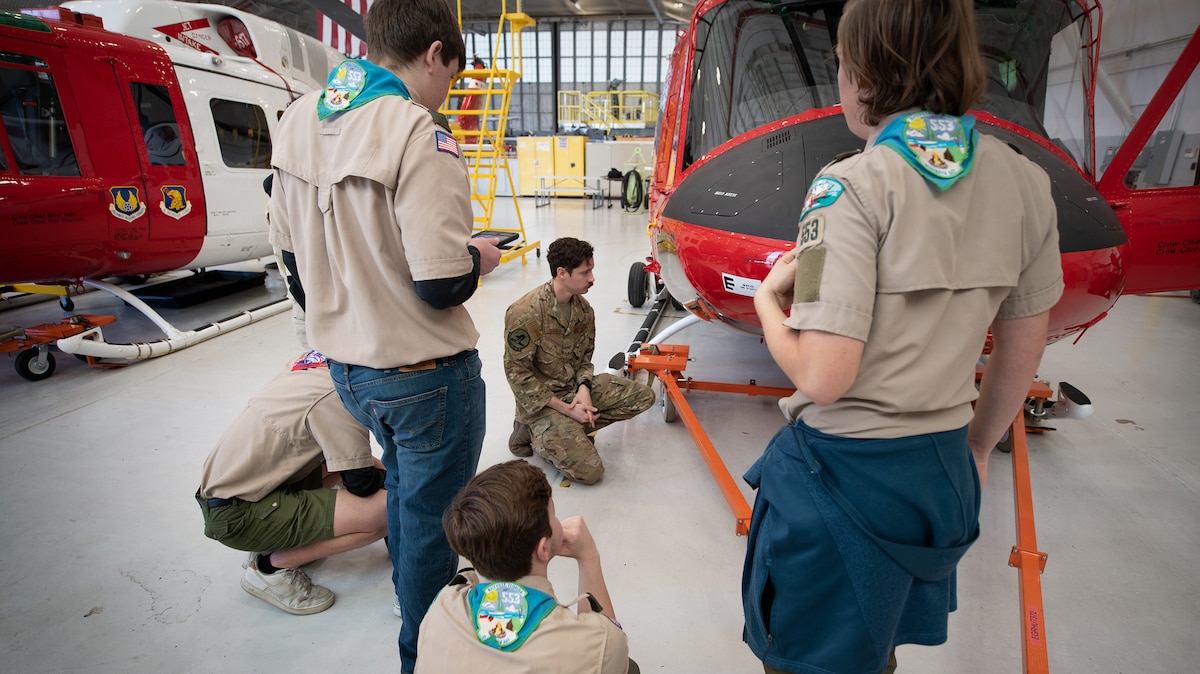 Scouts gather around the UH-1N Huey helicopter inside an aircraft hangar.