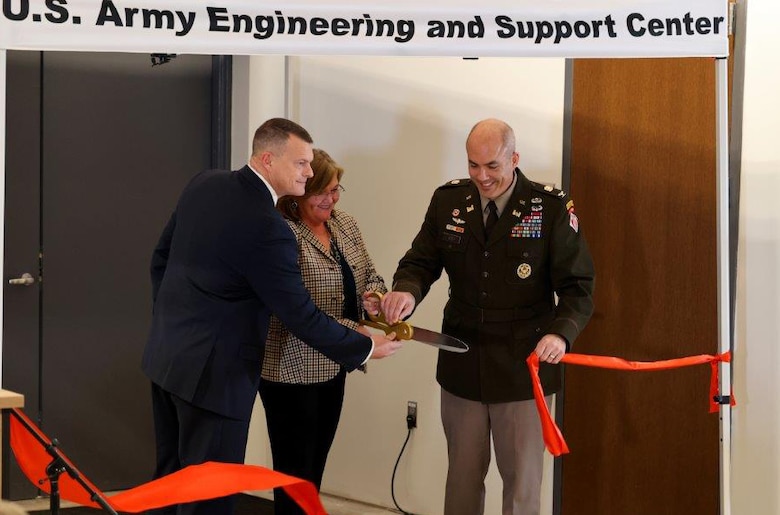 Army Colonel and two employees cut a ribbon.
