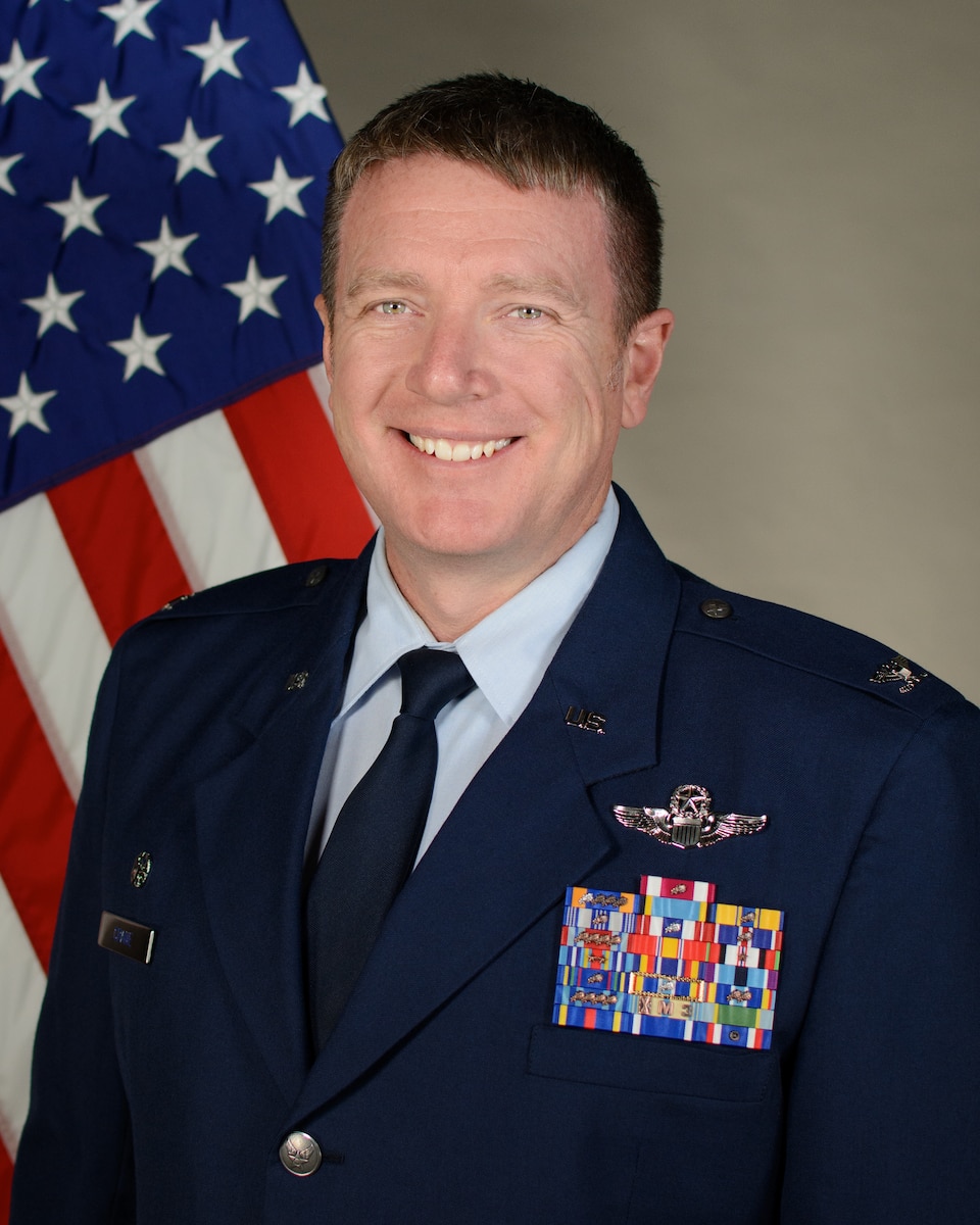 Service member smiles for official portrait in front of US flag wearing their service dress blues