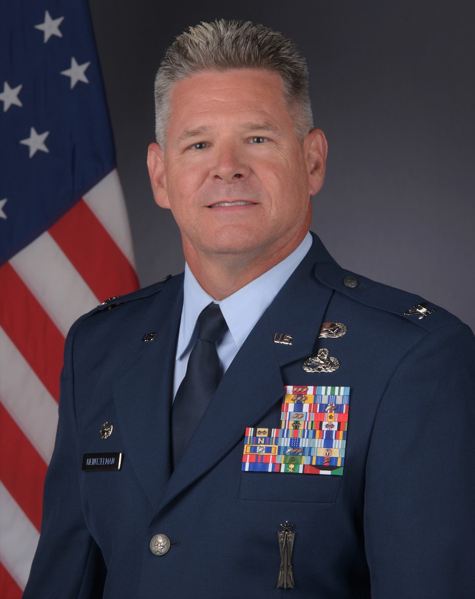 A man in service dress with a U.S. flag behind him.