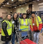 Five people in yellow safety vest pose in front of shopping cart.