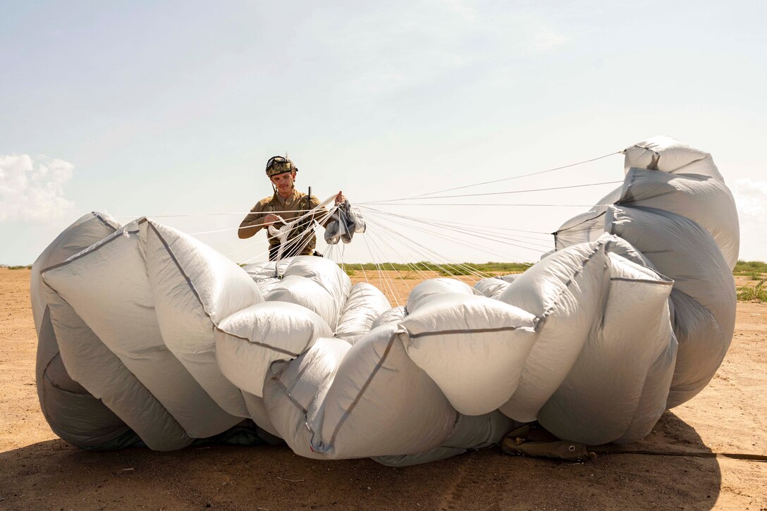 An airman gathers a parachute in a desert-like area.