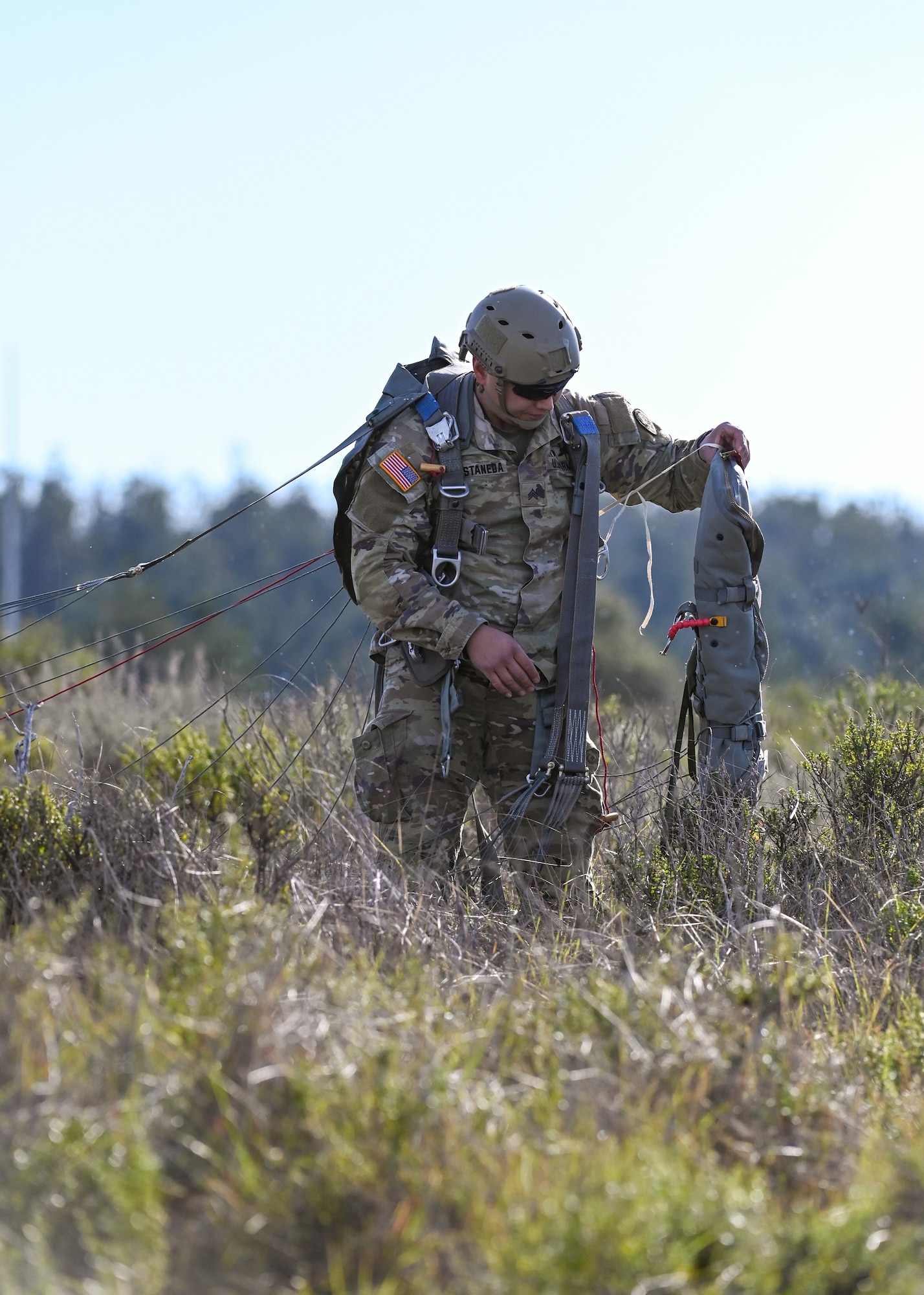 U.S. Army Reserve Sgt. Marco Castaneda packs up his parachute in the grassland landscape of Vandenberg