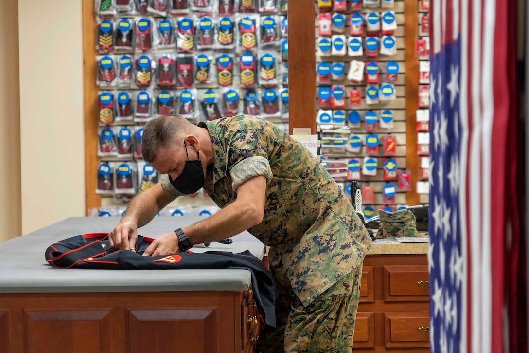 A Marine leans over to closely inspect a service dress uniform with American Flags hanging behind him.