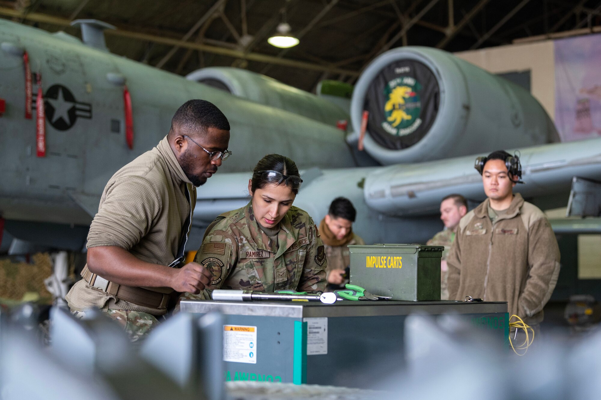 U.S. Air Force Senior Airman Kenny Segobia and Airman 1st Class Monique Ramirez, 25th Fighter Generation Squadron weapons load crew members, prepare to load munitions onto an A-10C Thunderbolt II during a weapons load crew of the quarter competition at Osan Air Base, Republic of Korea, Jan. 5, 2024. As part of the competition, teams are evaluated on how quickly and efficiently they can inspect and load munitions onto their respective aircraft. (U.S. Air Force photo by Staff Sgt. Aubree Owens)