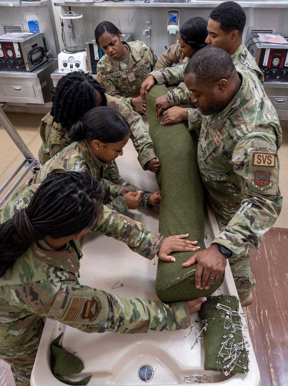 Seven airmen flank the sides of a mannequin while tucking in the ends of the green cloth wrapping.