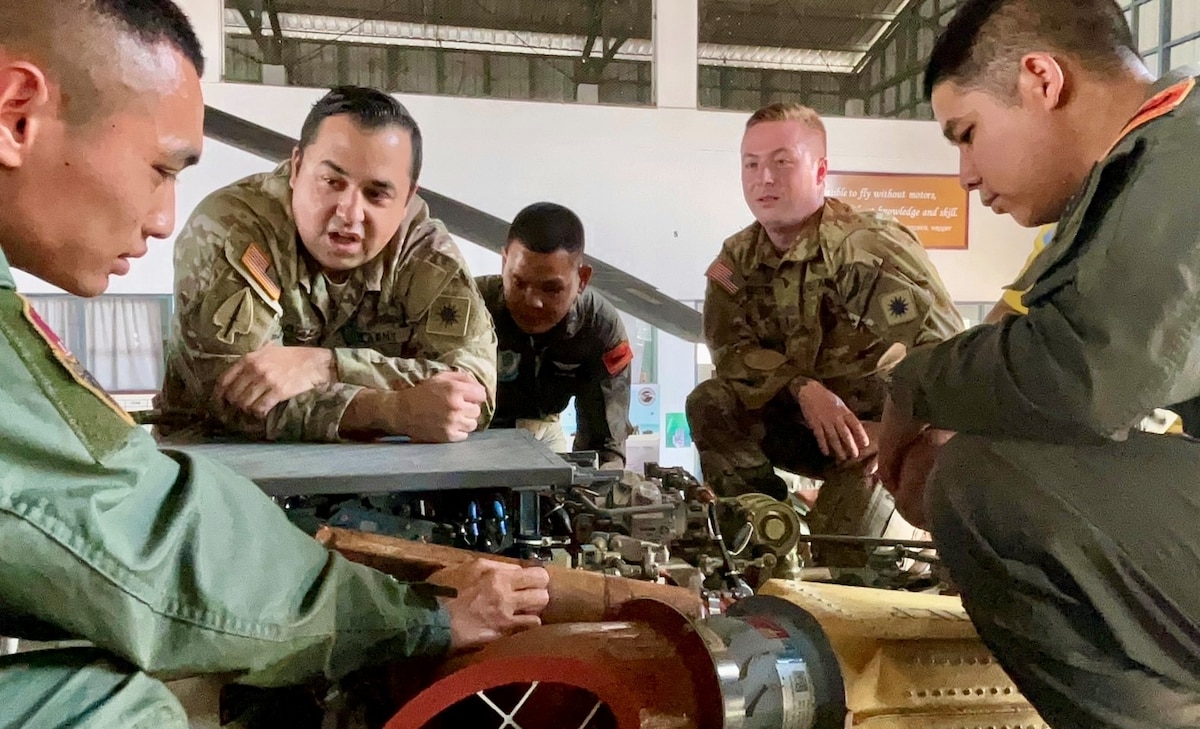 Chief Warrant Officer 2 Chris Cuddington and Sgt. Richard Diaz, 1st Battalion, 168th General Support Aviation, Washington National Guard, talk with Royal Thai Army Aviation members about aircraft hydraulics during a subject matter expert exchange in December 2023 in Lopburi, Kingdom of Thailand. The Washington National Guard and Thailand are partners in the State Partnership Program.