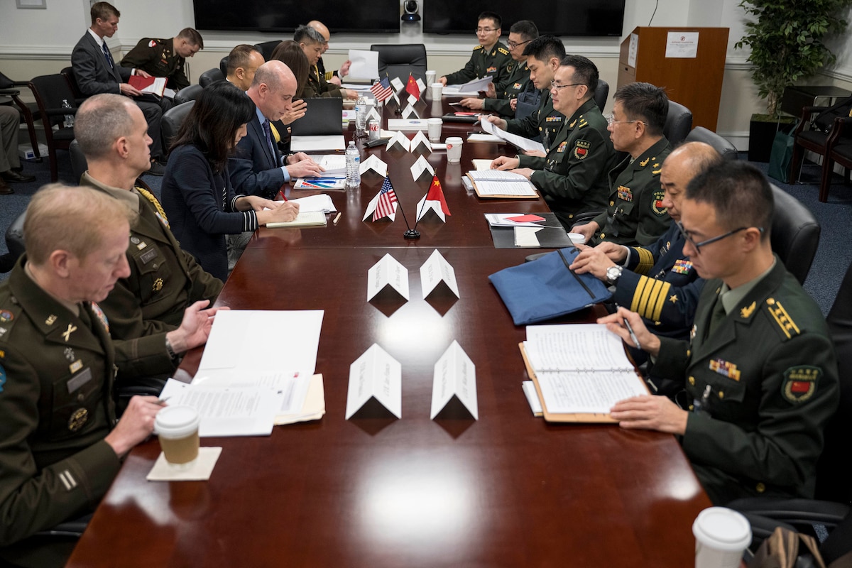 People sit at a table with U.S. and Chinese flags.