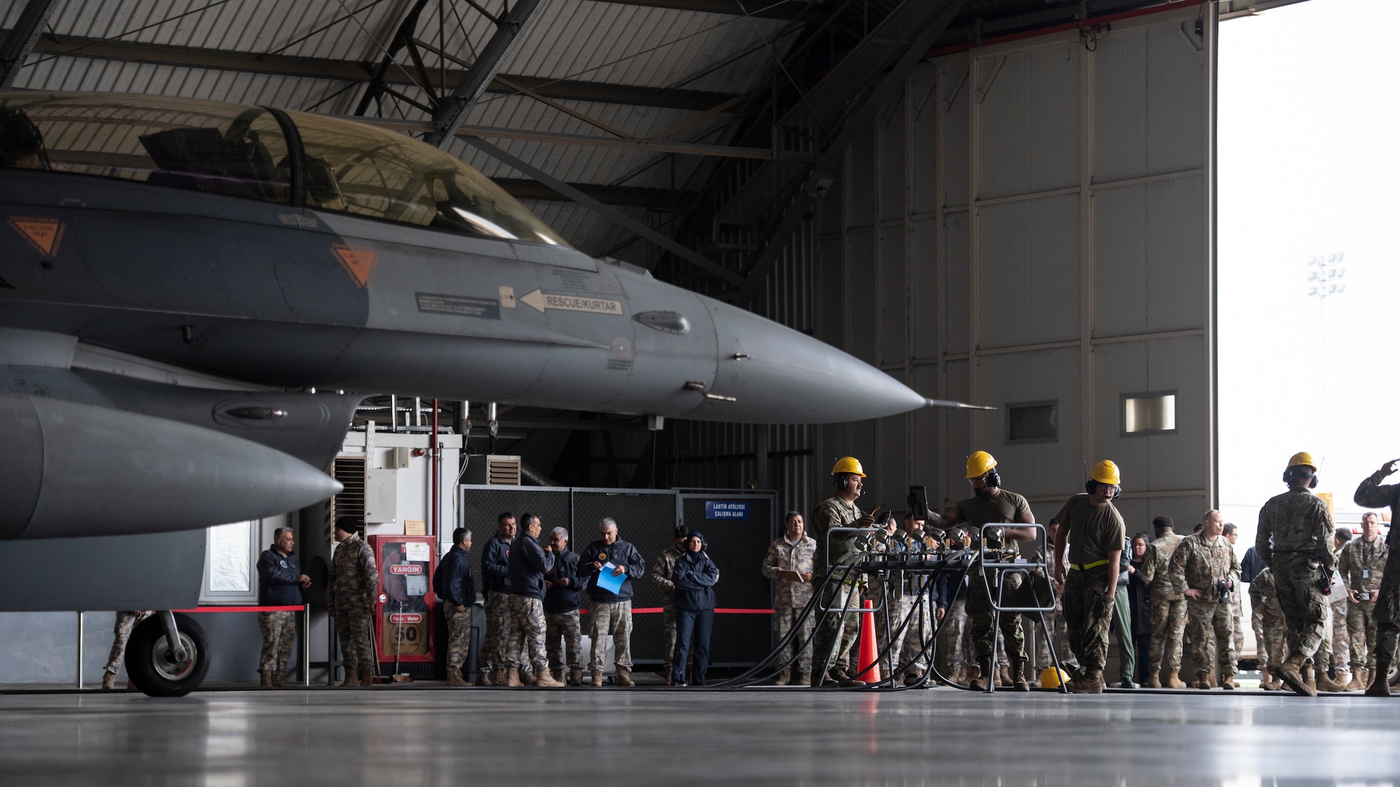 An F-16 inside a hangar with U.S. and Turkish air force members conducting a Crash Damaged or Disabled Aircraft Recovery exercise