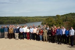 A large group of people stand together in front of a lake.