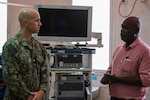 A Navy officer and a doctor speak in front of medical equipment in an office setting.