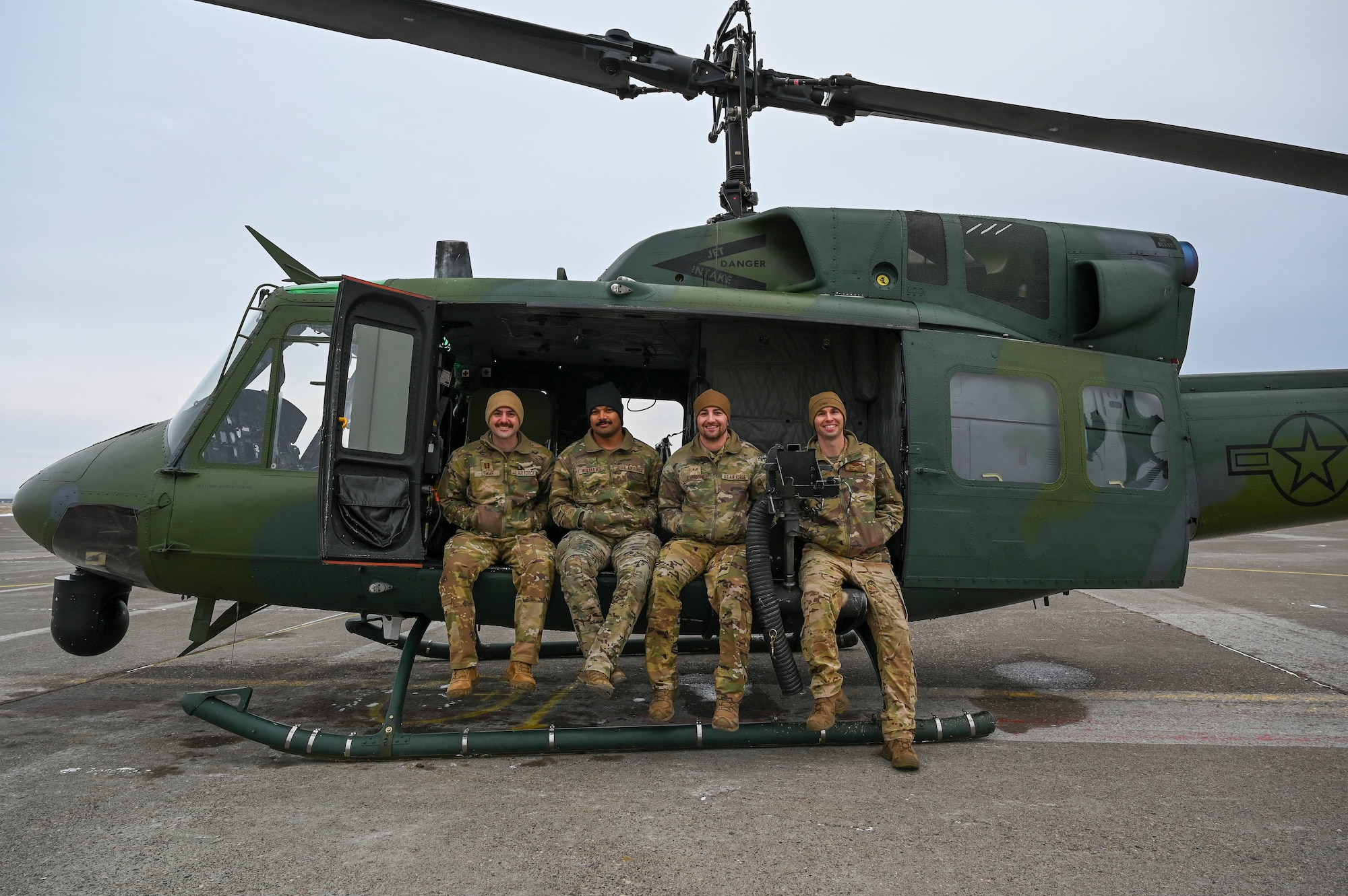 Four Airmen sitting in a helicopter on the ground.