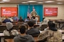 A man in a United States Army uniform stands at a podium in front of high school students.