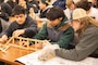 Three students sit at a desk and build a model dam out of toothpicks.