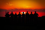 A silhouettes photo illustration of eight soldiers standing in a row with a vivid red and orange sky behind them.