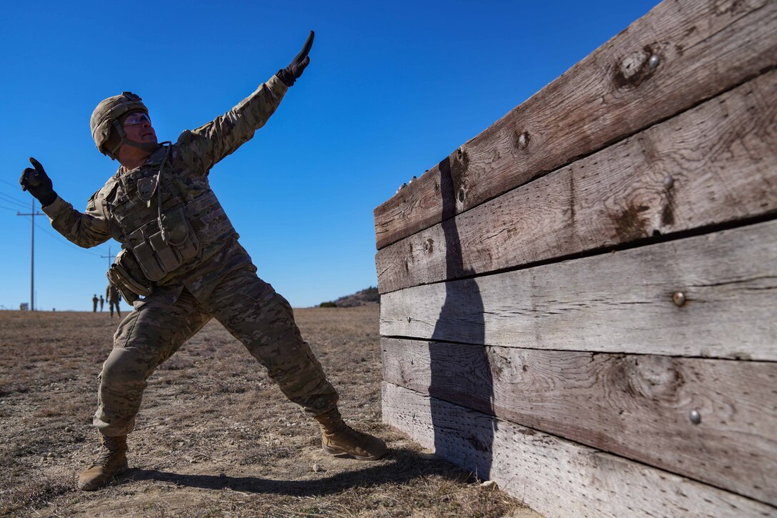 A soldier prepares to throw a grenade over an obstacle.