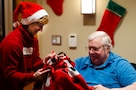 woman wearing Christmas outfit shares a blanket with man sitting in a chair.