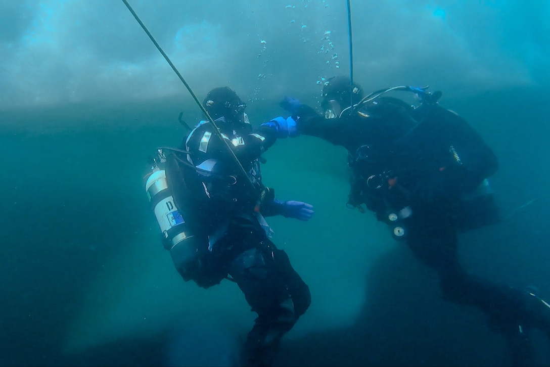Two Coast Guard divers bump fists underwater.