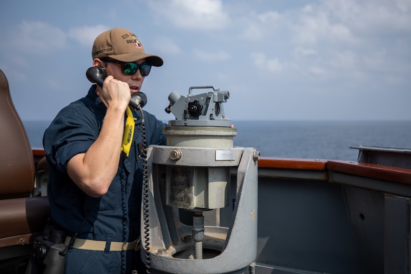 A person in uniform holds a phone to his ear aboard a ship at sea.