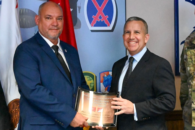 Two men shake hands while holding an award.