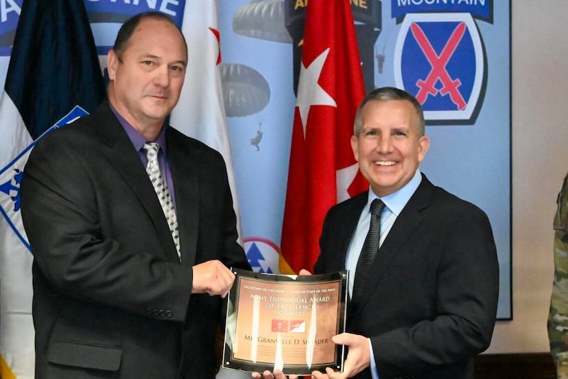 Two men shake hands while holding an award.