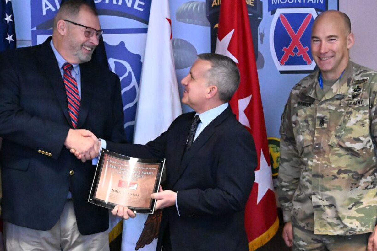 Two men shake hands while holding an award.