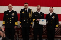 A photo of a man with a certificate on a stage.