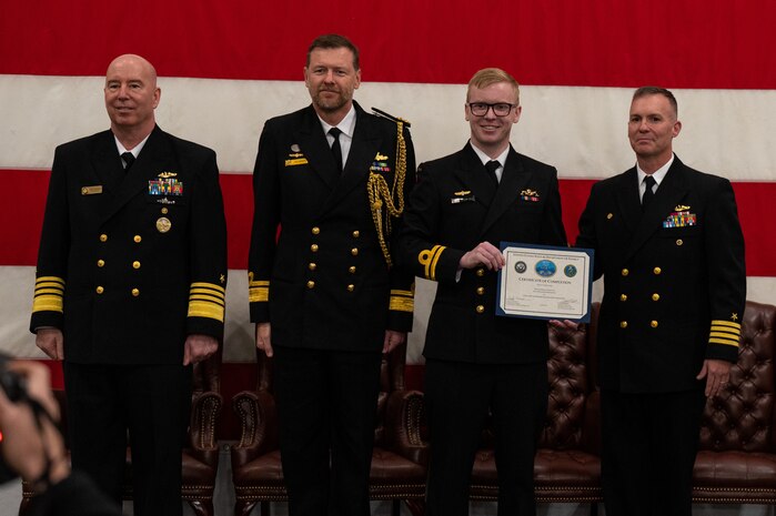 A photo of a man with a certificate on a stage.