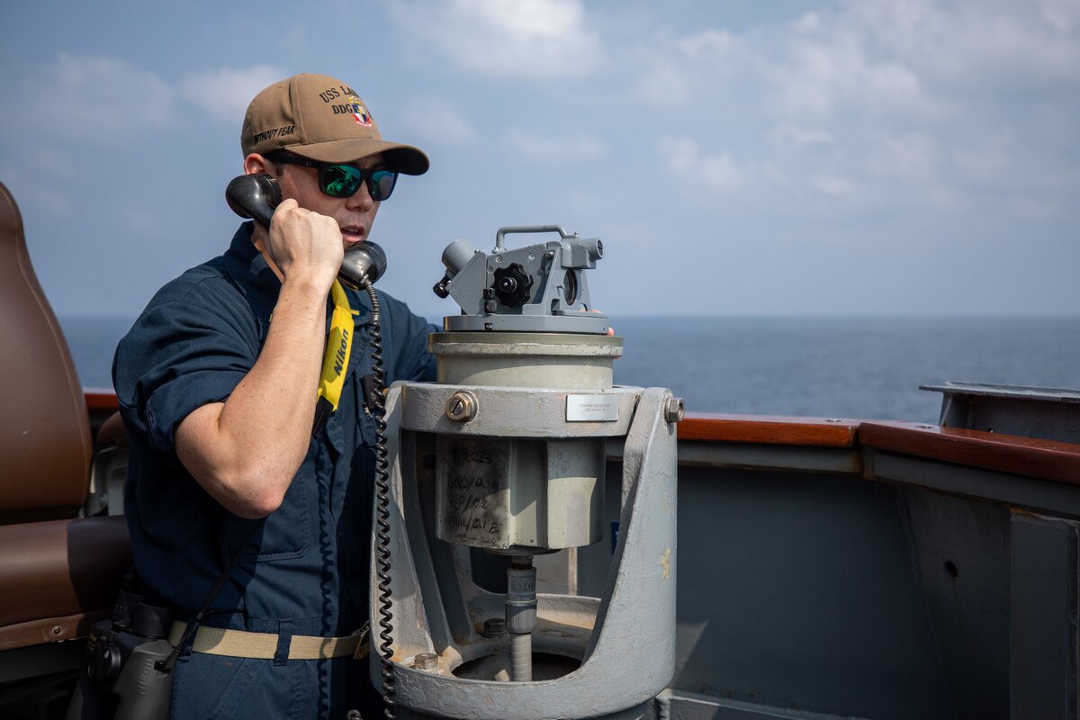A person in uniform holds a phone to his ear aboard a ship at sea.