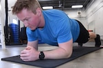 U.S. Air National Guard Technical Sgt. Devon Parr, a 185th Air Refueling Wing aerospace propulsion technician, demonstrates a forearm plank at the 185th Air Refueling Wing in Sioux City, Iowa, Jan. 11, 2024. Airmen must pass routine physical health assessments which include a core endurance component tested by one minute timed situp, two minute cross leg reverse crunch or timed forearm plank. (U.S. Air National Guard photo illustration by Senior Airman Tylon Chapman)