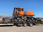 A tracked vehicle with a snowplow sits on a flatbed trailer.