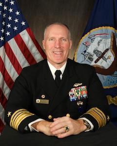 Vice Adm. Robert Gaucher poses for an official portrait in front of the National Ensign and the Navy flags.