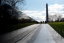 A long view of the Vietnam Veterans Memorial, with the Washington Monument and a group of people in the distance.
