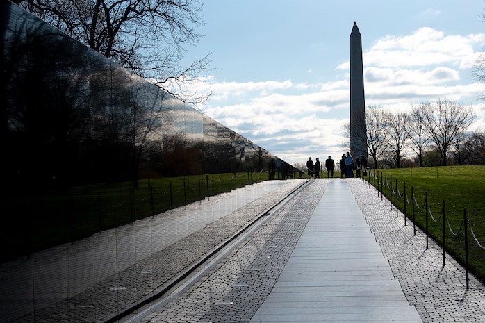 A long view of the Vietnam Veterans Memorial, with the Washington Monument and a group of people in the distance.