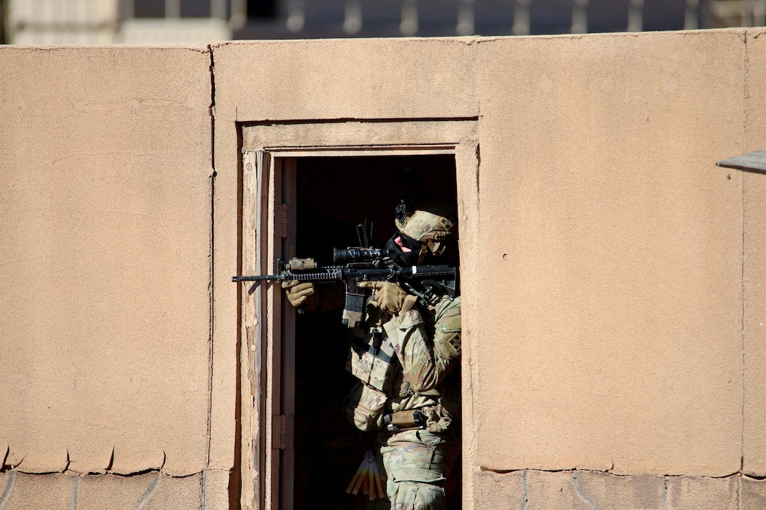 A soldier stands in a doorway aiming a weapon.