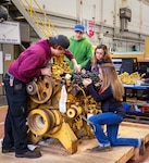 Joshua Buffington, mechanic helper; Benjamin Early and Janelle Sorensen, Heavy Mobile equipment mechanic apprentices; and Hannah Honeycutt, mechanic helper, Code 730, Lifting and Handling Crane Maintenance Division; perform valve adjustment checks on a diesel engine from a portal crane, at Puget Sound Naval Shipyard & Intermediate Maintenance Facility in Bremerton, Washington. (U.S Navy photo by Wendy Hallmark)