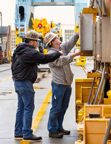 Keith Ryan, mechanic helper, Code 730, Crane Maintenance, and Mitch Urrutia, crane inspector, Code 721, Inspection, Test, Quality Assurance, and Training Division, inspect the contents of a portal crane gantry box Dec. 14, 2023. (U.S Navy Photo by Wendy Hallmark)