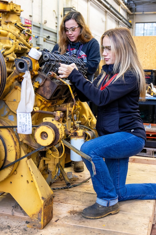 Hannah Honeycutt, mechanic helper, and Janelle Sorensen, heavy mobile equipment mechanic apprentice, Code 730, Crane Maintenance, perform valve adjustment checks on an engine. (U.S Navy Photo by Wendy Hallmark)